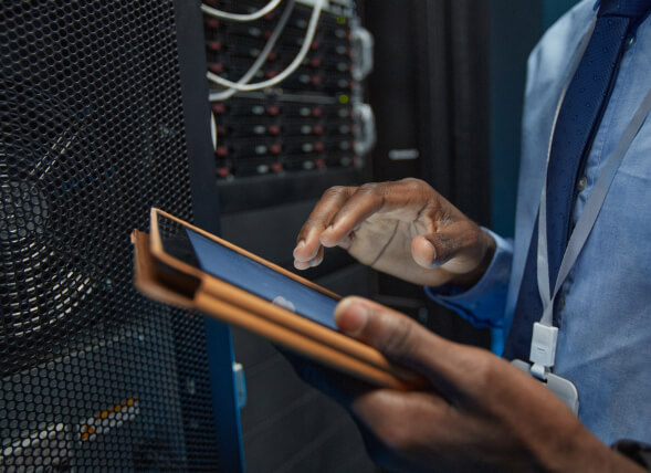 close-up-african-american-man-holding-digital-tablet-while-standing-by-server-cabinet-working-with-supercomputer-data-center img